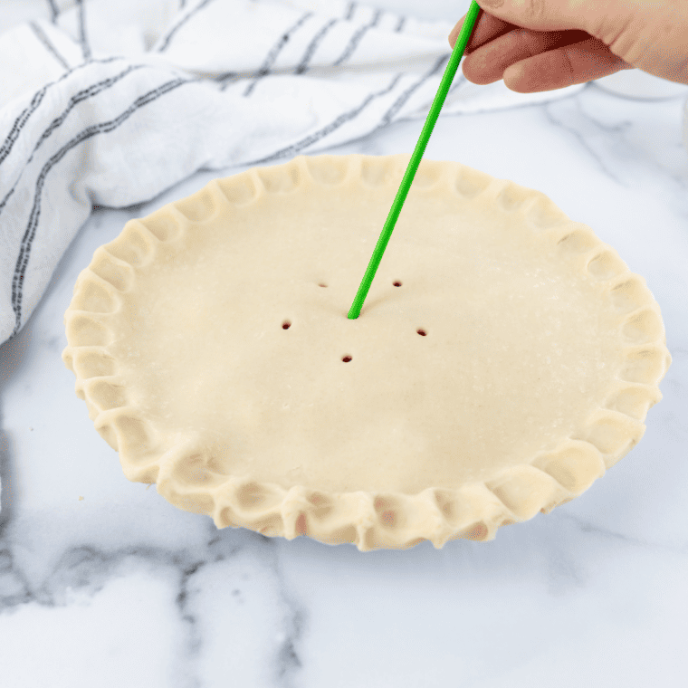 Laying the second pie crust over the cherry filling and cutting slits to vent steam