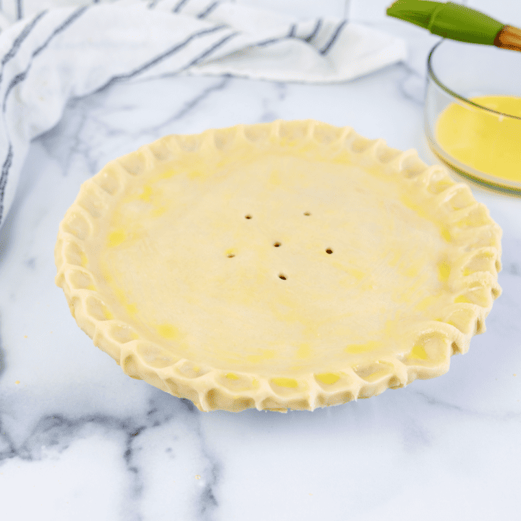 Brushing egg wash over the top crust of the cherry pie before air frying