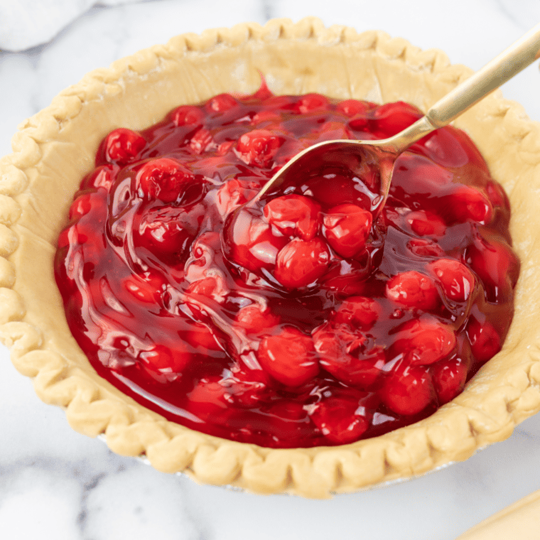 Spooning cherry pie filling into the bottom crust and spreading it evenly