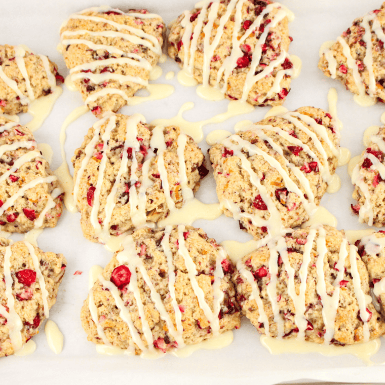 Baked cranberry orange scones being drizzled with orange glaze
