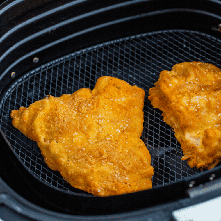 Golden brown battered fish cooking in air fryer basket with tartar sauce and fries ready to serve.