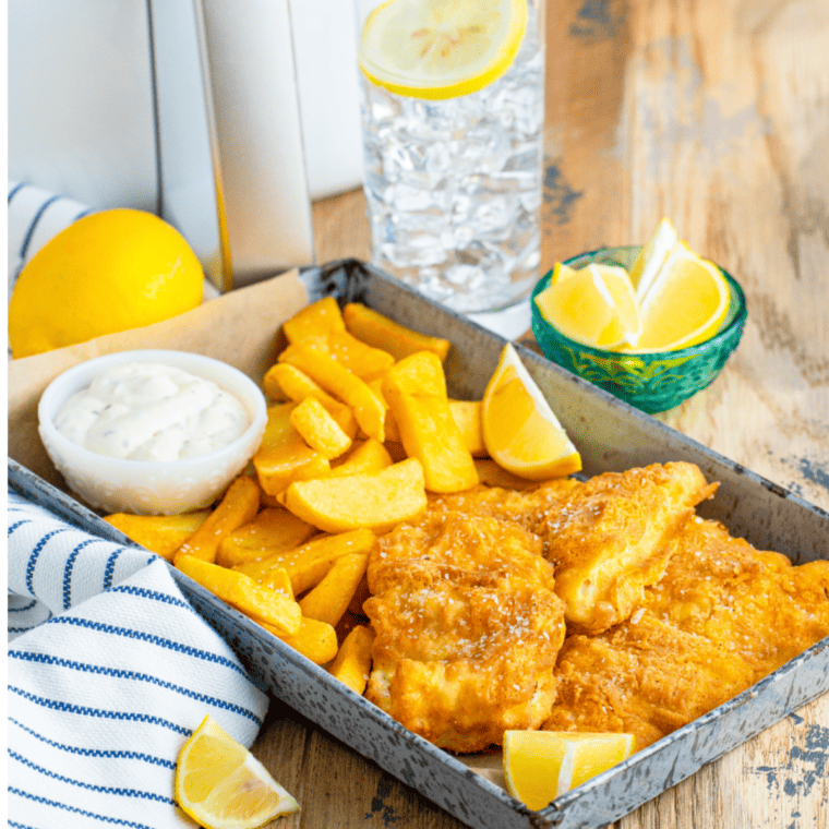 Crispy air fryer fish and chips served with lemon wedges and tartar sauce on a plate.