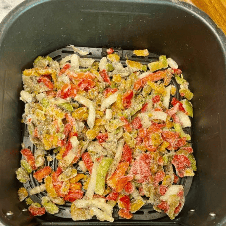 Air Fryer Frozen Peppers and Onions cooking in the air fryer basket.