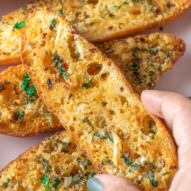 Air fryer basket filled with toasted garlic bread brushed with butter and sprinkled with fresh herbs.