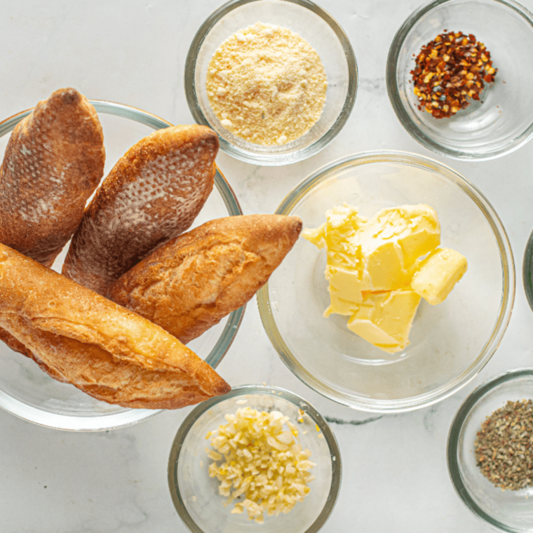 Ingredients for air fryer garlic bread: butter, fresh garlic, parsley, oregano, parmesan, and a sliced baguette.