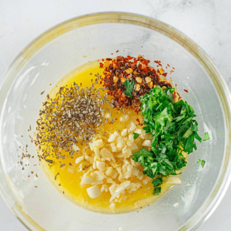 Mashing fresh herb garlic butter in a small white bowl.