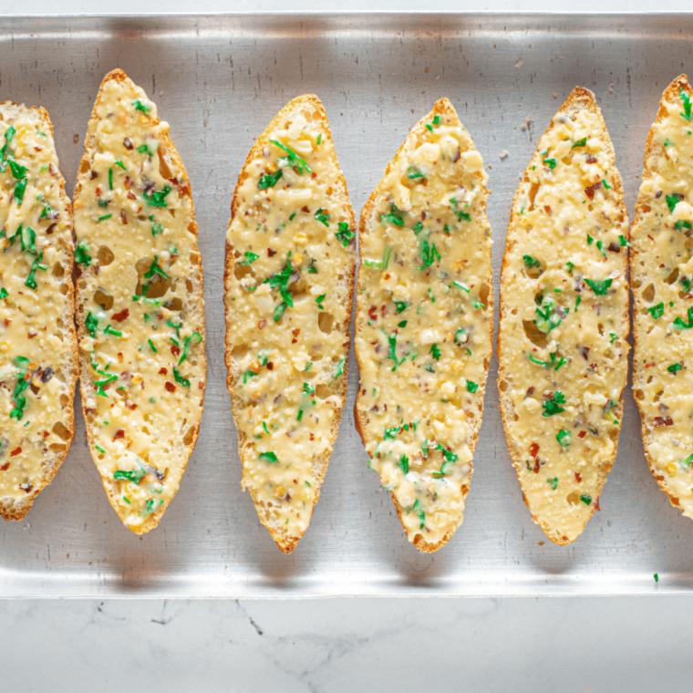 Spreading herb garlic butter onto sliced baguette pieces.