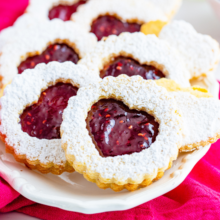 Golden, crispy Air Fryer Linzer Cookies filled with sweet fruit jam and dusted with powdered sugar on a plate.