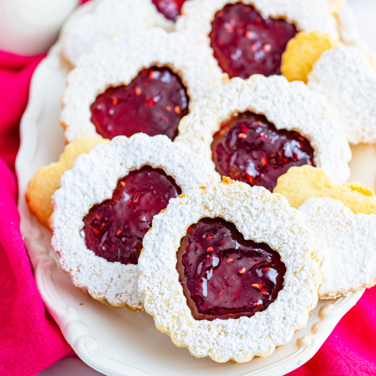 A batch of golden-brown Air Fryer Linzer Cookies with raspberry preserves filling, dusted with powdered sugar.
