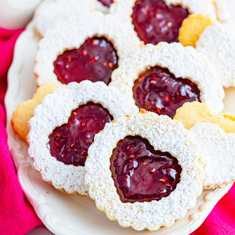 Close-up of golden, crispy Air Fryer Linzer Cookies filled with raspberry jam and dusted with powdered sugar on a plate.