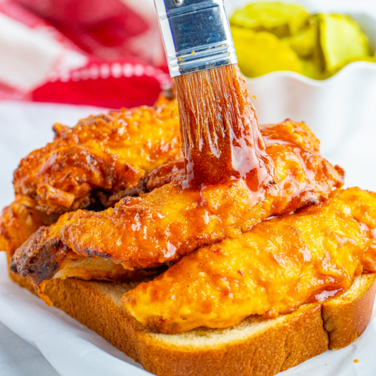 Stack of air fryer Nashville hot chicken tenders with glossy red hot sauce and dill pickle chips on top