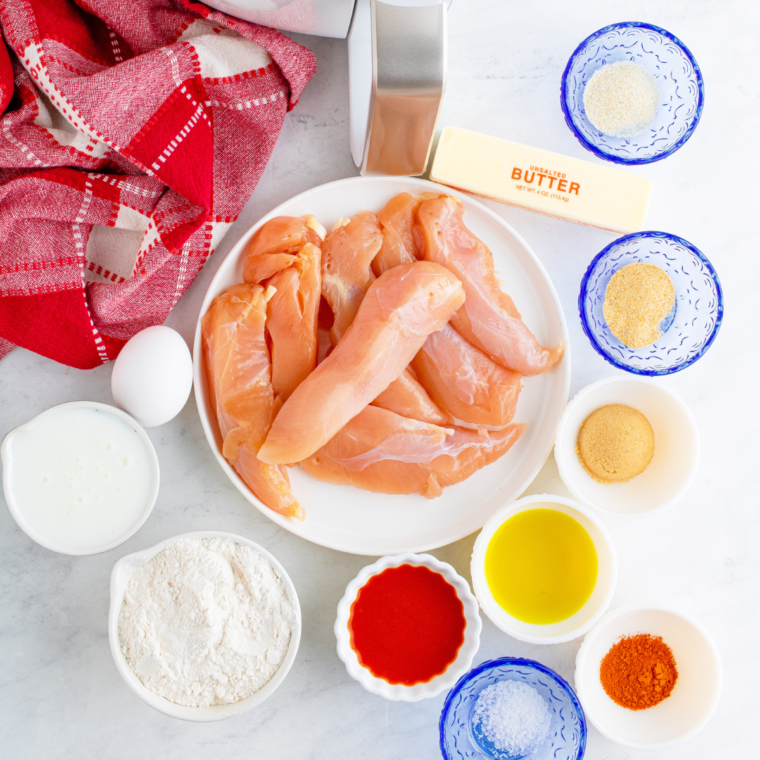 Ingredients for air fryer Nashville hot chicken tenders including chicken tenderloins, buttermilk, pickle juice, cayenne pepper, brown sugar, flour, and spices arranged on a wood board