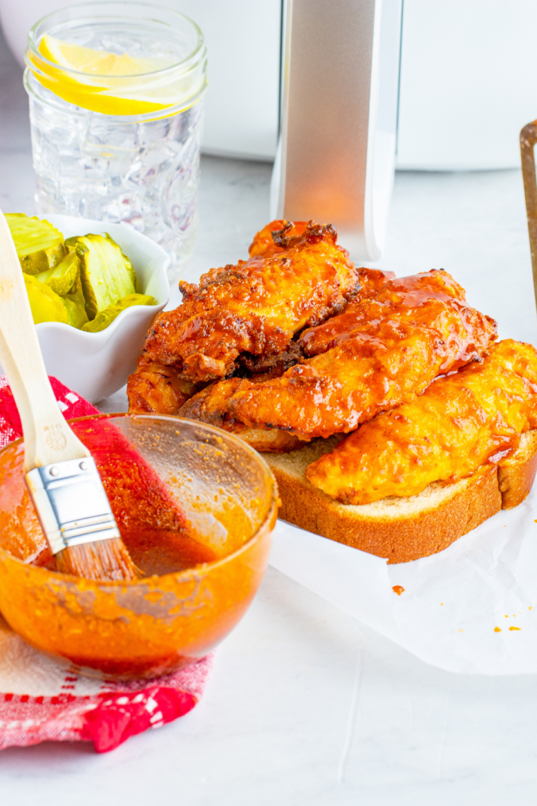 Hand dipping a crispy Nashville hot chicken tender into ranch dressing with the spicy red glaze visible on the crust