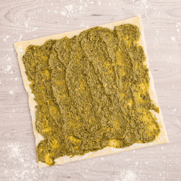 Spreading pesto sauce on a sheet of puff pastry for Air Fryer Pesto Pinwheels.
