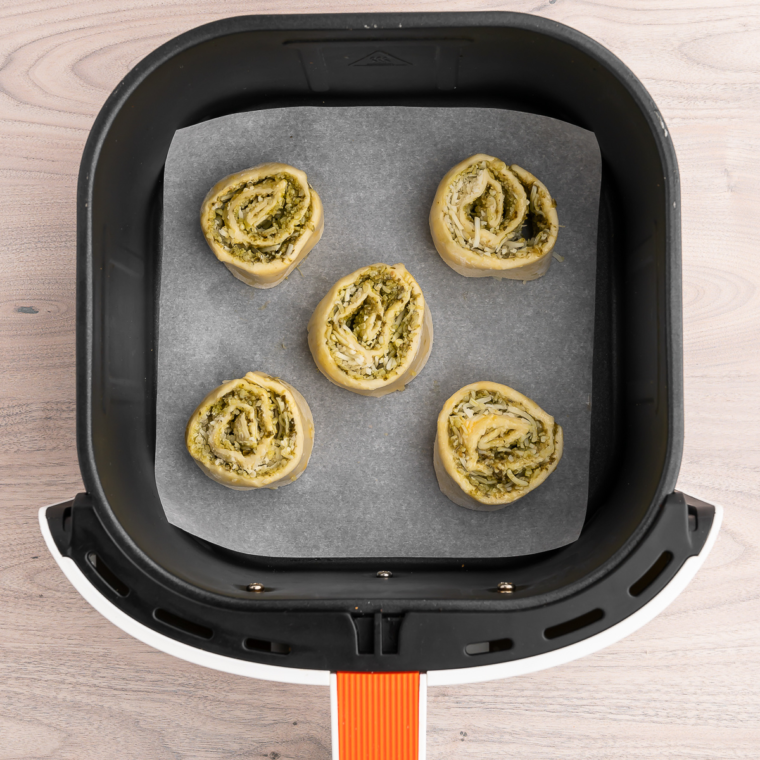 Placing Air Fryer Pesto Pinwheels in the air fryer basket for cooking."