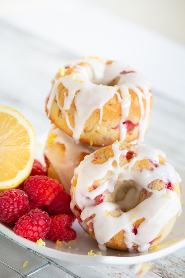 Plate of air fryer raspberry lemon donuts with glaze and fresh raspberries