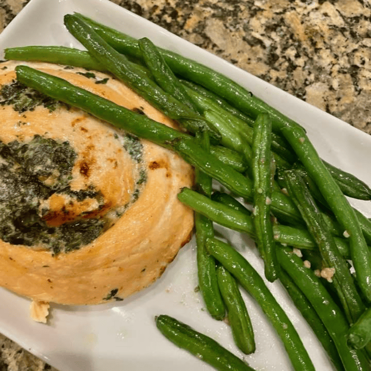 Cooked Trader Joe’s salmon pinwheels filled with spinach and herb cheese, served with roasted vegetables on a white plate.