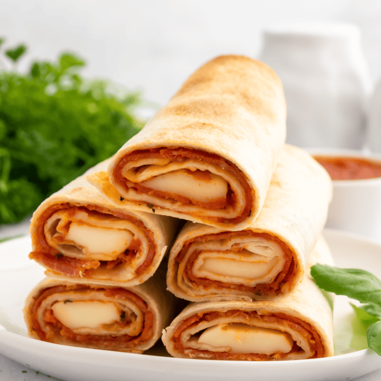 Plate of golden-brown Air Fryer Pizza Roll Ups filled with cheese and pepperoni, garnished with fresh basil.