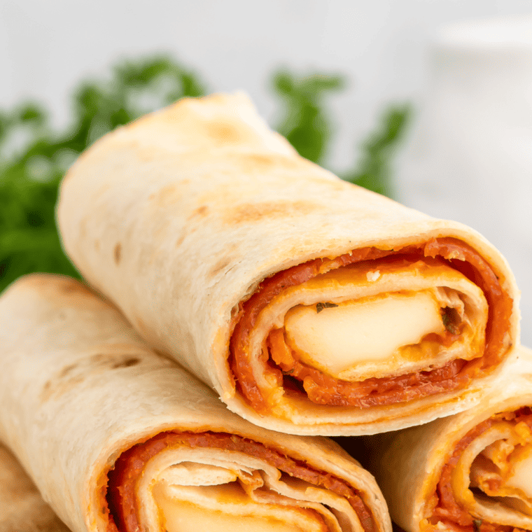 "Plate of golden-brown Air Fryer Pizza Roll Ups stuffed with cheese and pepperoni, garnished with parsley and served with a side of marinara sauce for dipping."