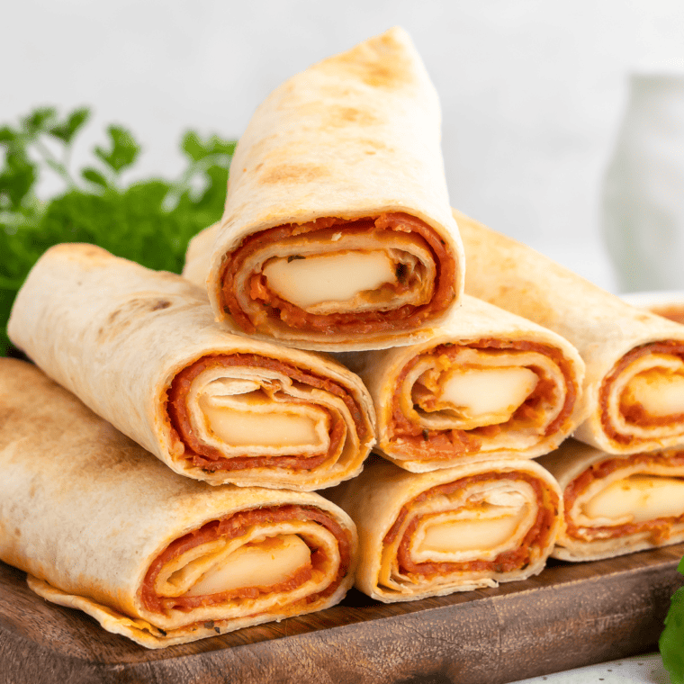 Image of finished Air Fryer Pizza Roll Ups on a plate: "Golden-brown Air Fryer Pizza Roll Ups stuffed with cheese and pepperoni, served on a white plate with marinara sauce for dipping."