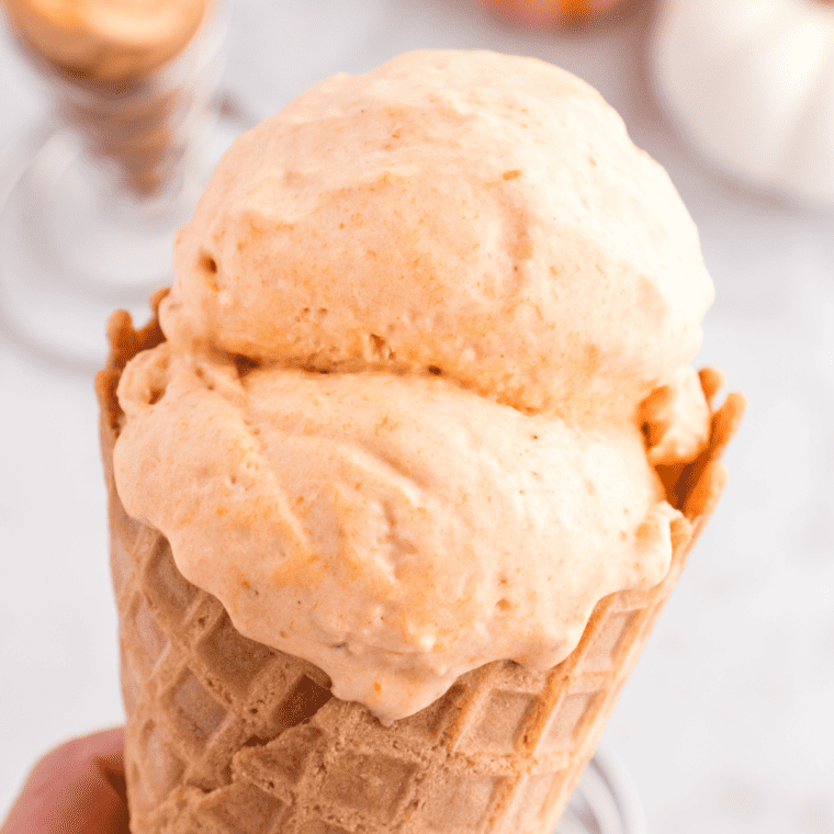 Two scoops of homemade pumpkin ice cream in a glass dish with a spoon