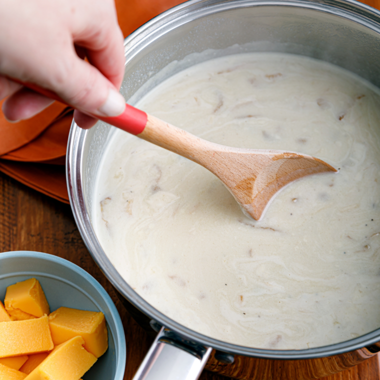 Pouring chicken and beef broth into a pot with flour and caramelized onions, stirring to create a smooth, clump-free mixture.