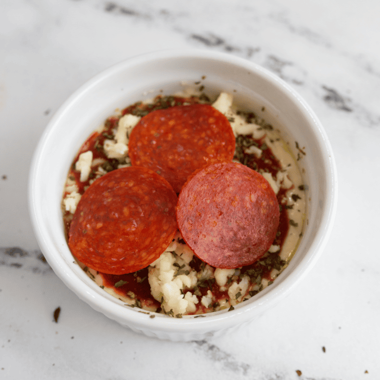 Layering cheese and toppings in a dish for Air Fryer Pizza Dip.
