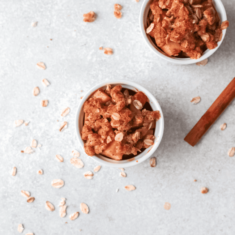 A bowl of warm apple crisp topped with a scoop of vanilla ice cream and a sprinkle of cinnamon.