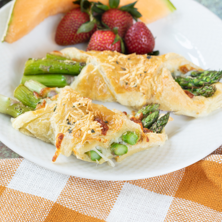Close up of Asparagus Puff Pastry Bundles on kitchen table. with strawberries on white plate.
