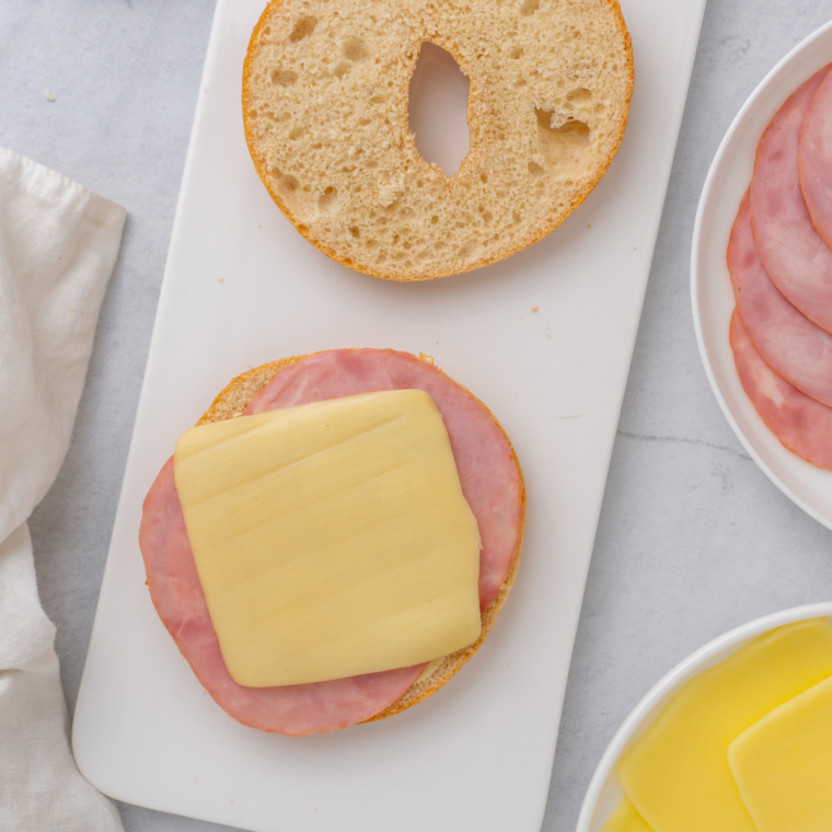 Assembling the breakfast sliders by layering cheese, cooked bacon or sausage, and eggs on the toasted bagels