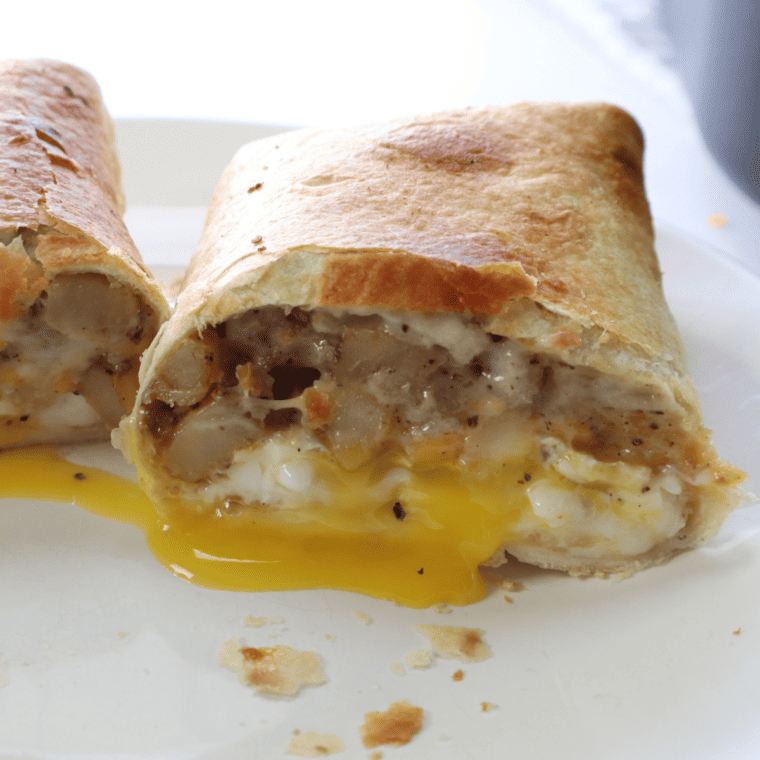A close-up of an Air Fryer Barn Yard Buster Wrap, showcasing layers of crispy bacon, juicy sausage, fluffy scrambled eggs, and creamy gravy wrapped in a soft tortilla.