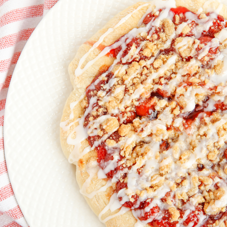 Close-up of cherry dessert pizza with golden crust and white icing drizzle on a plate