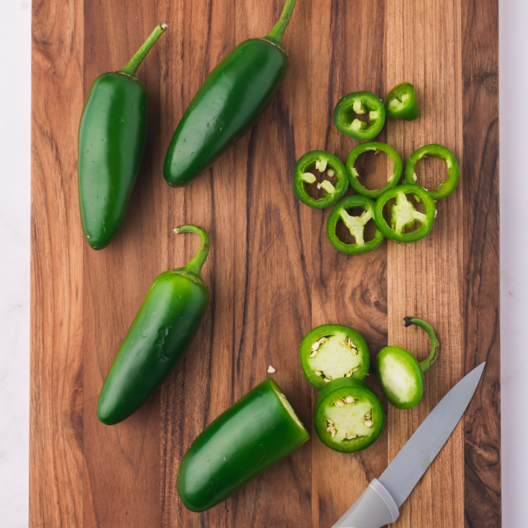 Fresh jalapeños being washed, dried, and sliced into rounds on a cutting board.