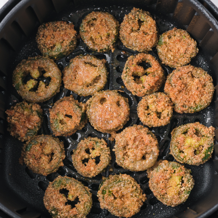 Arranging breaded jalapeño slices in a single layer in the air fryer basket, ready to be air fried.