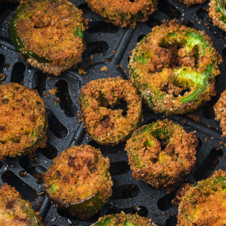 Golden, crispy air-fried jalapeño slices served on a plate with a side of dipping sauce.
