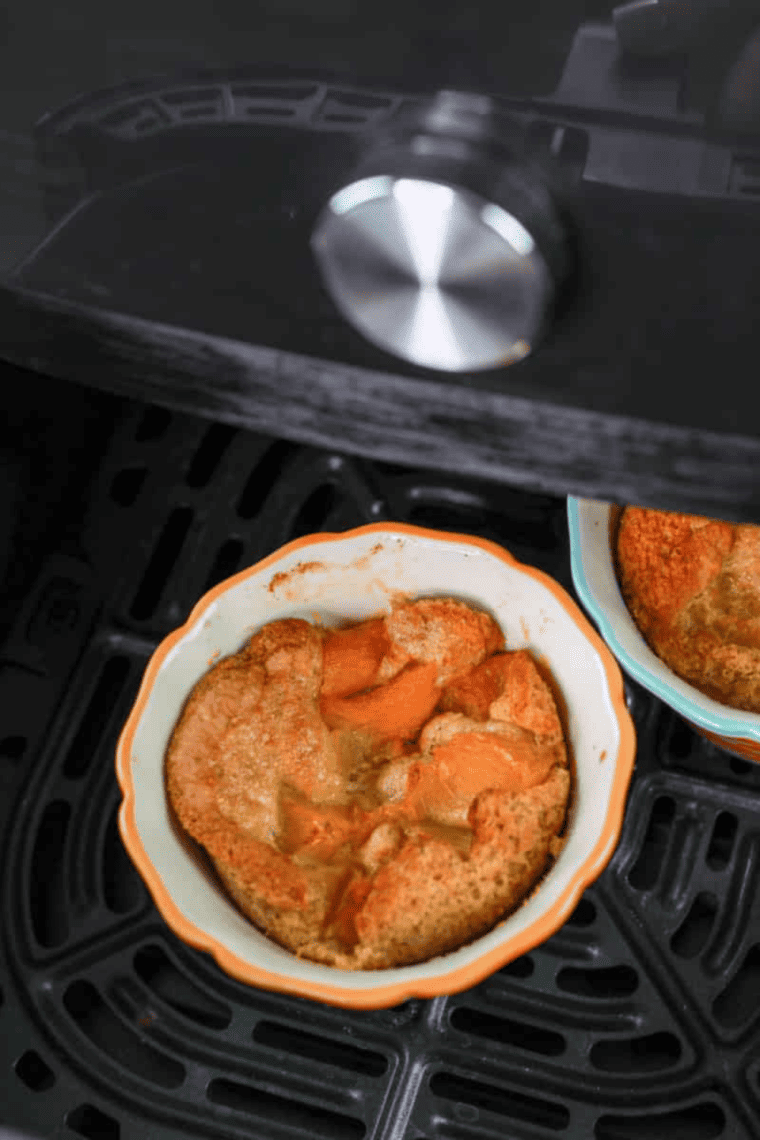 Mug filled with golden-brown peach cobbler cooked in an air fryer, topped with a scoop of vanilla ice cream.