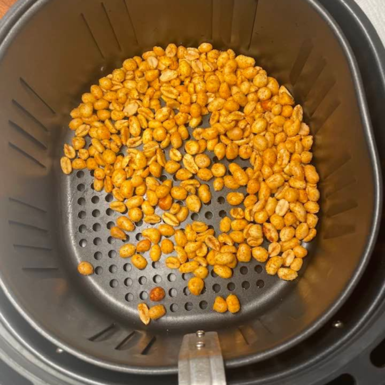 Spreading seasoned peanuts on baking sheet or in the air fryer basket before roasting.
