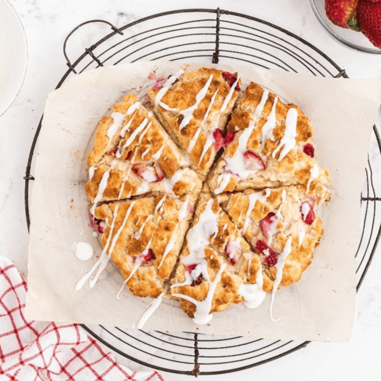 A plate of golden-brown Air Fryer Strawberry Scones with fresh strawberry pieces and a drizzle of glaze.