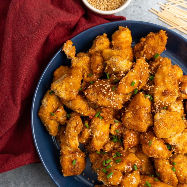 Air Fryer Sweet Chili Chicken Bites garnished with sesame seeds and green onions, served on a plate.