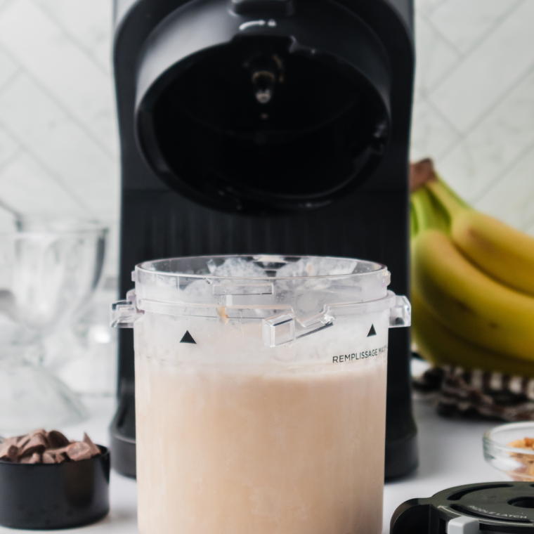 Ninja Creami machine processing ice cream, with a spoon creating a hole in the center of the frozen pint.