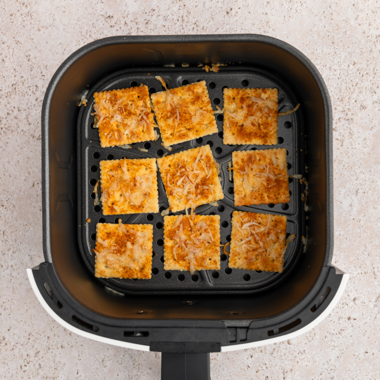 Cheesy saltine crackers arranged in air fryer basket cooking until melted and bubbly