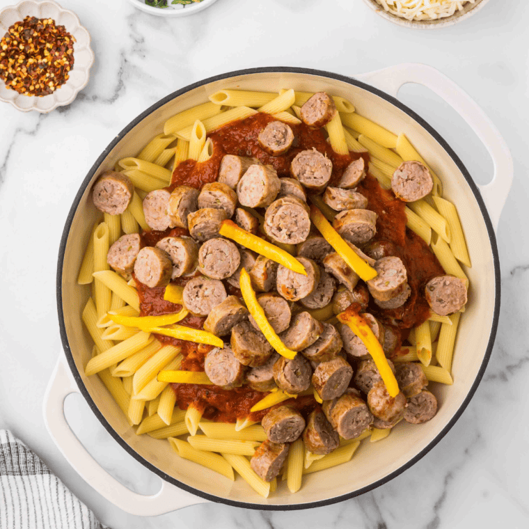Marinara sauce being poured from jar into skillet over sausage and peppers.