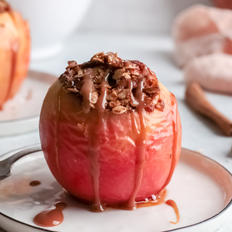 Air fryer baked apples being carefully removed from the basket, served warm with vanilla ice cream, caramel drizzle, and whipped cream on top.