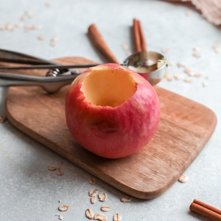 Apples being cored with a melon baller, removing seeds and stem while keeping bottom intact to form a hollow cavity.