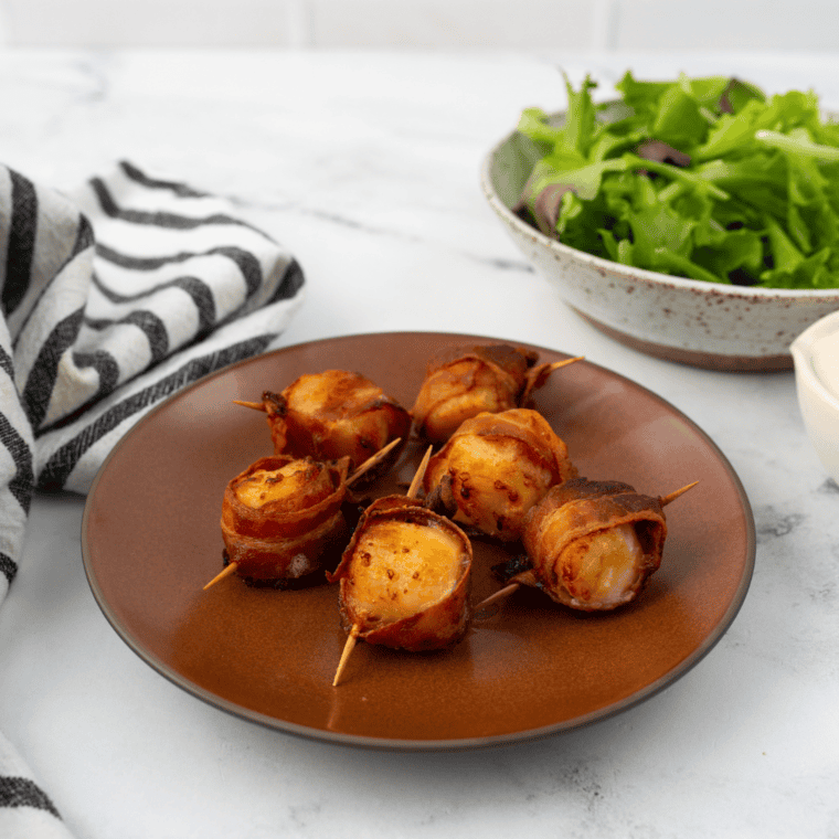 Golden-brown frozen scallops wrapped in crispy bacon, cooked in an air fryer, served on a plate.