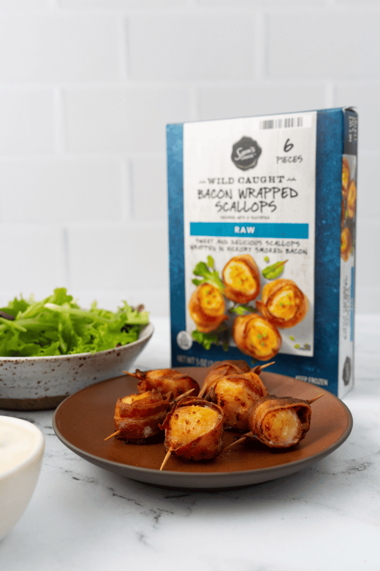 Crispy air fryer frozen bacon-wrapped scallops served on a plate, garnished with herbs.