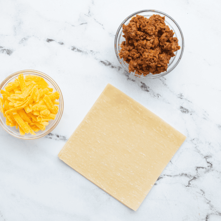 Ingredients for Air Fryer Taco Bell Wontons, including wonton wrappers, seasoned ground beef, shredded cheese, and dipping sauce.