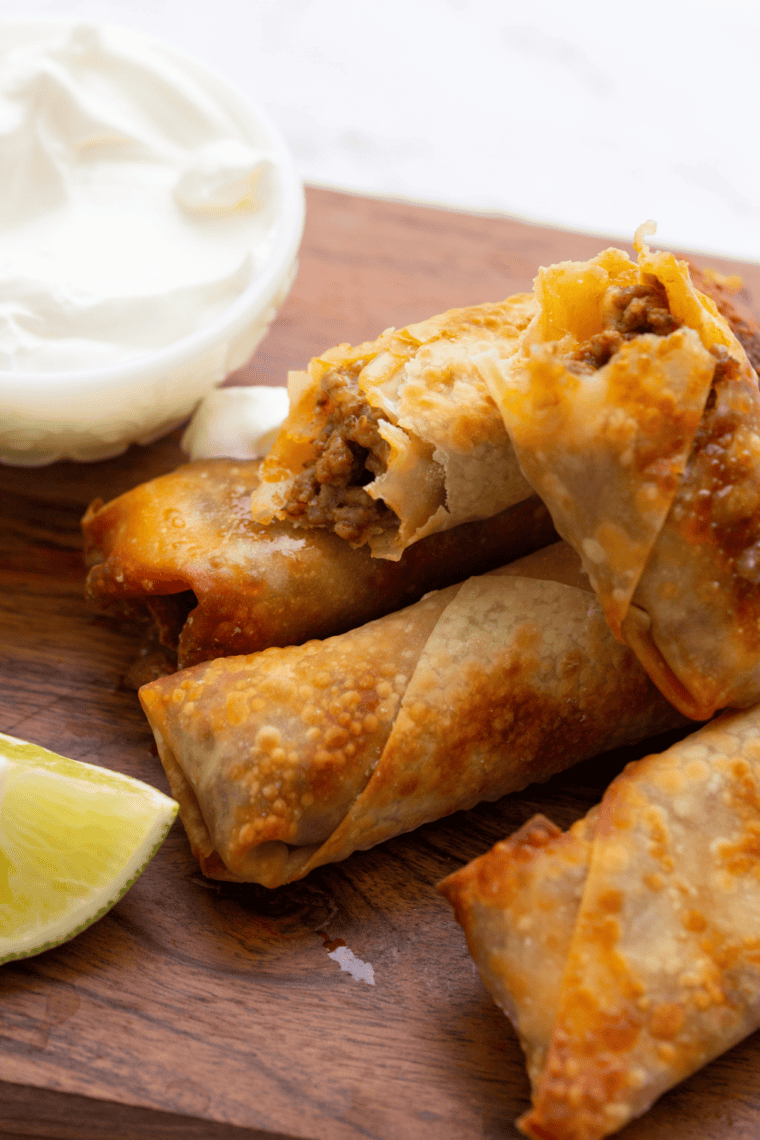 A close-up image of crispy Air Fryer Taco Bell Wontons arranged on a plate, accompanied by a small bowl of dipping sauce and garnished with fresh herbs.
