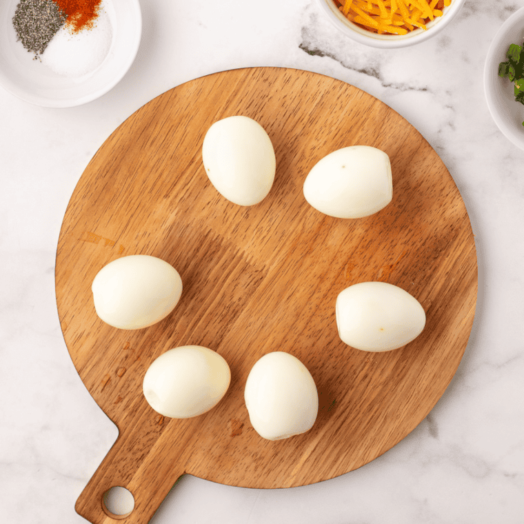 Hard-boiled eggs being peeled and sliced in half with the yolks separated into a bowl