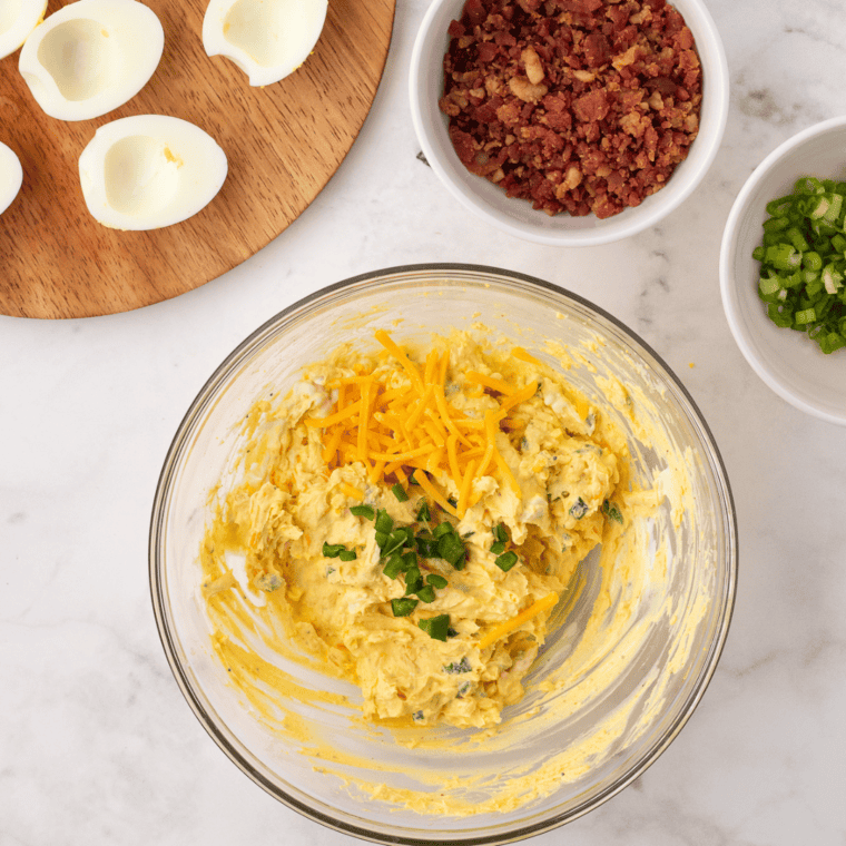Creamy deviled egg filling being mashed smooth in a glass mixing bowl